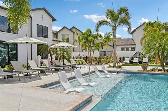 A pool with chairs and umbrellas in front of a building at The Hadley - North Port, FL Apartments, North Port, FL