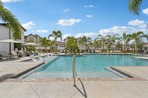A pool surrounded by palm trees and lounge chairs. at The Hadley - North Port, FL Apartments, North Port