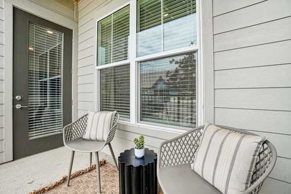 A patio with a chair, a couch, and a table with a potted plant on it.