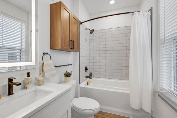 a white bathroom with white subway tile and a shower and a sink and a toilet at Meridian at CityPlace, Woodbury Minnesota