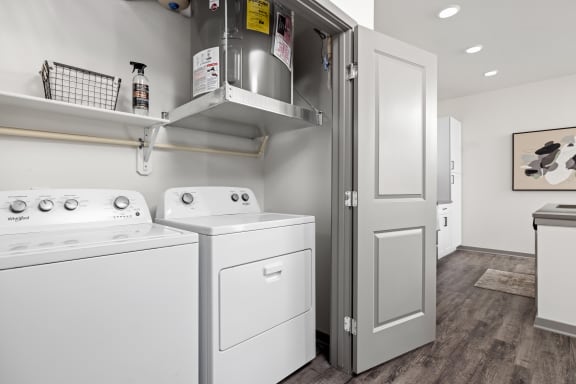 a white washer and dryer in a room with a refrigerator and a door at The Depot Luxury Apartment Homes, Raymore, MO