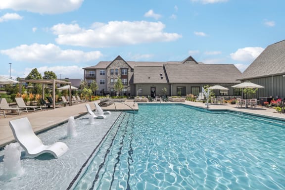 a swimming pool with chairs and a building in the background at The Depot in The Depot Raymore, MO 64083