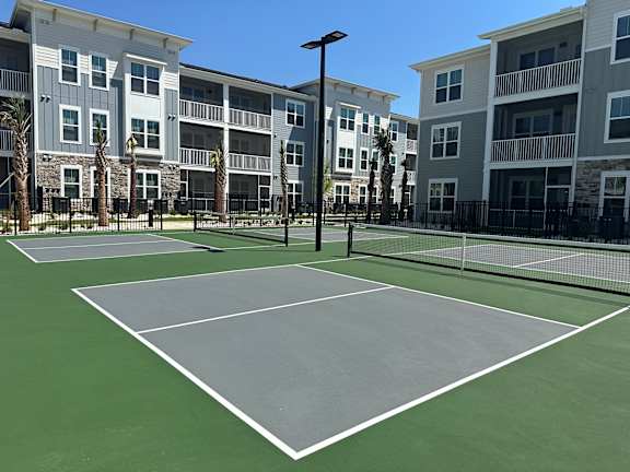 A tennis court is surrounded by apartment buildings.