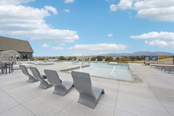 A pool surrounded by grey benches on a sunny day.at The Garrison Luxury Apartment Homes, Colorado, 80817