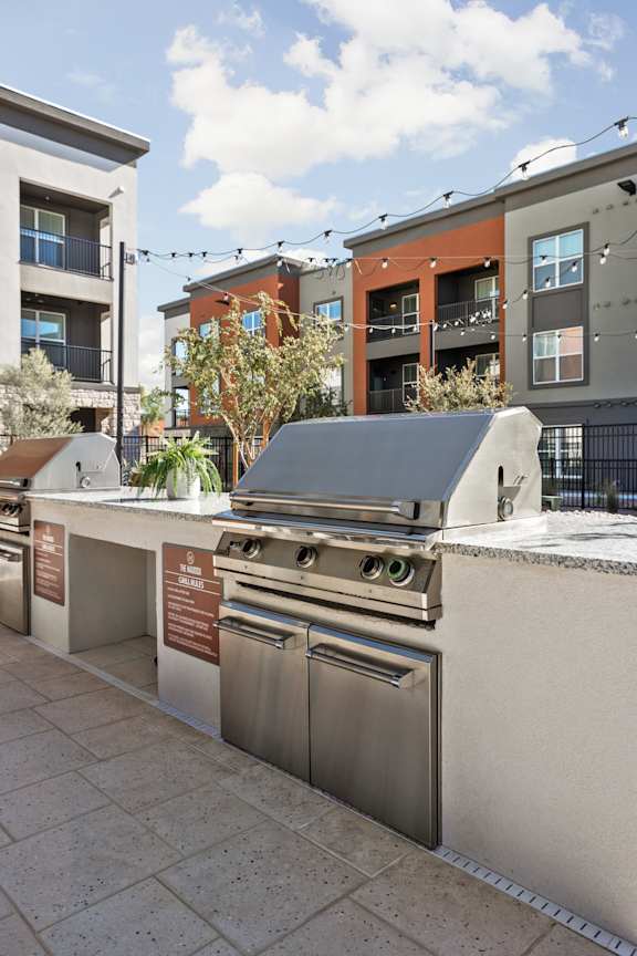 A row of outdoor stainless steel grills and ovens on a patio. at The Maddox Luxury Apartments, Buckeye, 85326