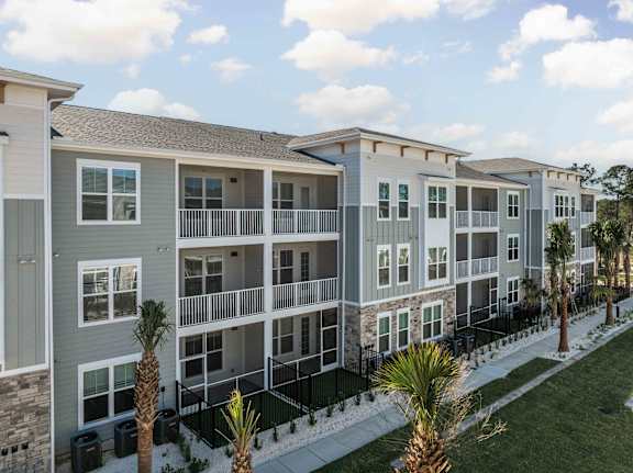 A row of modern apartment buildings with balconies and palm trees in front.