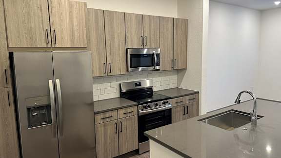 A kitchen with a stainless steel refrigerator, microwave, oven,  sink and cabinets.