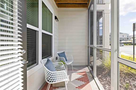 A white chair with a blue pillow is on a porch at Verity Luxury Apartments, Florida 32960