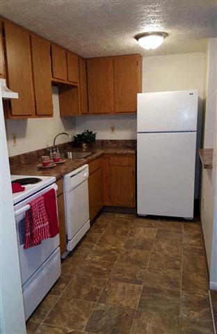 A kitchen with a white refrigerator and brown cabinets.