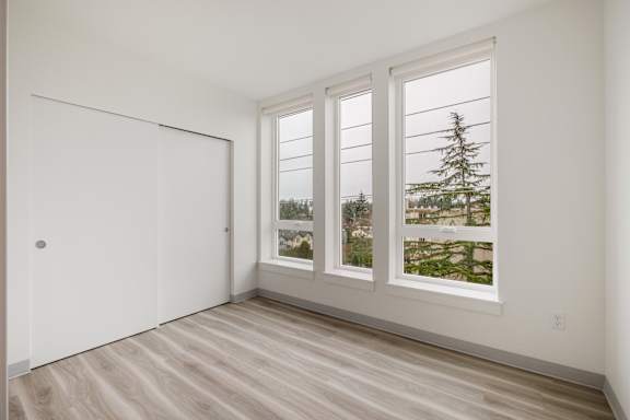 A room with a sliding door, hardwood floors, and a large window showing a view of trees and a building at Nook at Northaven Apartments, Washington, 98125