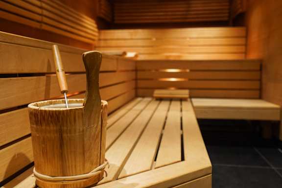 A wooden bucket with a wooden stick in it is placed on a wooden bench in a sauna.