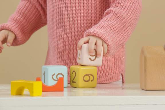 A child in a pink sweater is playing with numbered blocks.