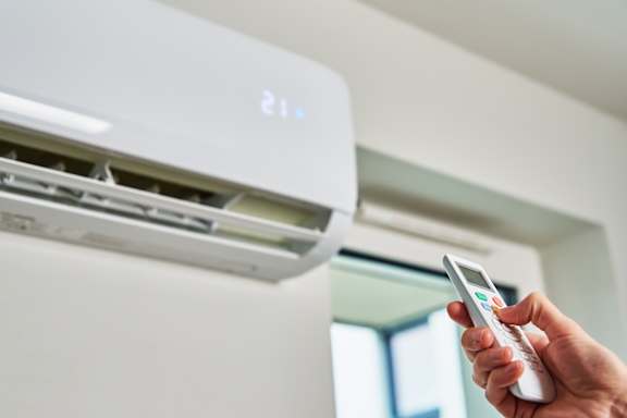 A person is holding a remote control in front of a white air conditioner.