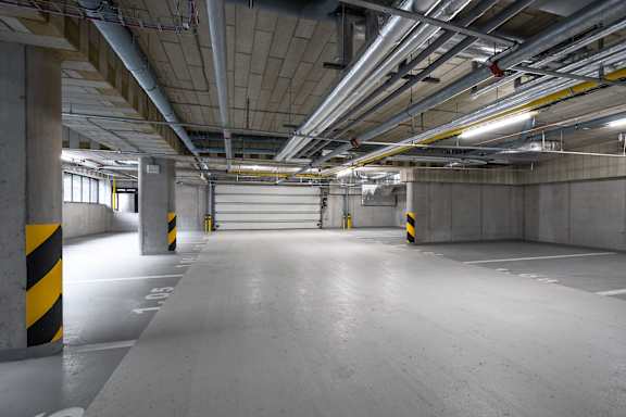 A spacious, empty parking garage with concrete pillars and yellow and black striped poles.