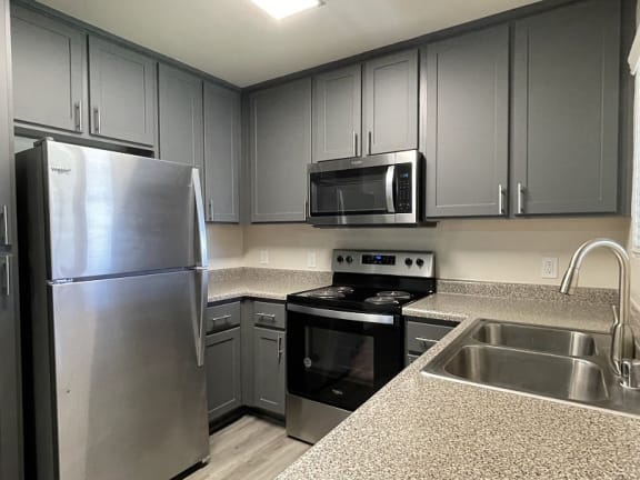 A kitchen with a stainless steel refrigerator, microwave, oven, and sink