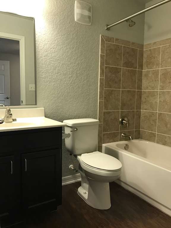 A white toilet in a bathroom with a white bathtub and brown tiles.
