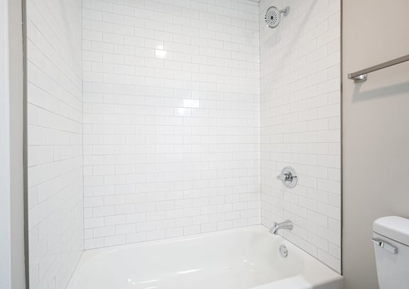 A white tiled bathroom with a white tub and toilet.