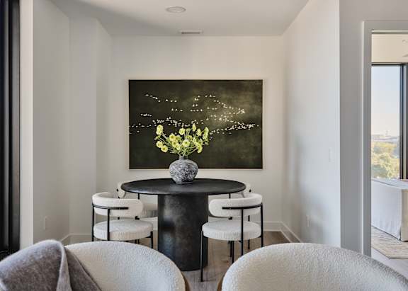 A painting of flowers is hanging on the wall above a table with chairs.