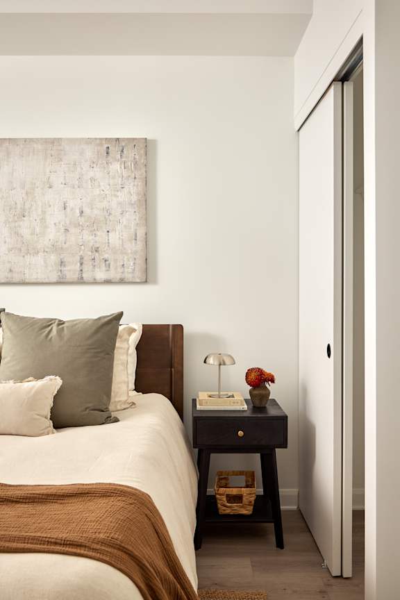 A bedroom with a bed, a table with a lamp, and a painting on the wall.