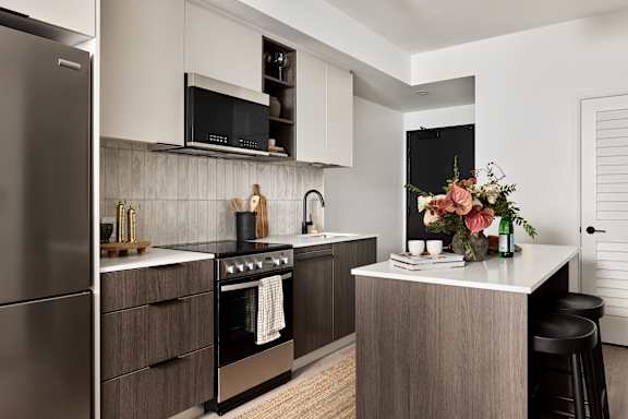 A modern kitchen with a stainless steel refrigerator and a central island with a bar stool.