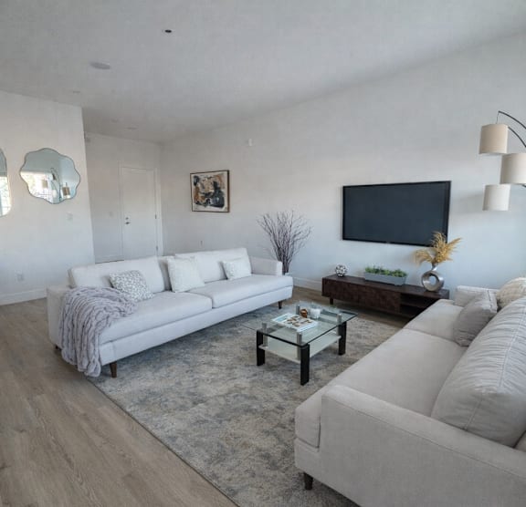 A living room with a white couch, a coffee table, and a flat screen TV mounted on the wall.