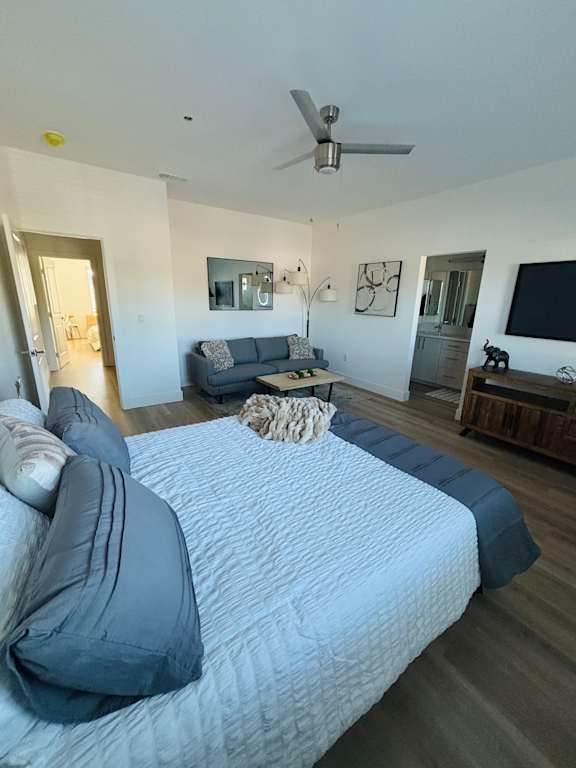 A bedroom with a bed, a couch, a ceiling fan, and a television.