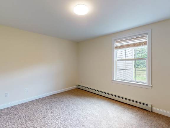 Empty bedroom with window and baseboard heater at Autumn Woods Apartments, Westbrook, ME