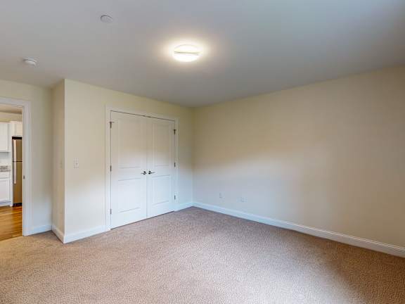 Empty carpeted bedroom with white closet doors at Autumn Woods Apartments, Westbrook, 04092