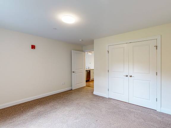 Empty carpeted bedroom with closet and hallway access at Autumn Woods Apartments, Westbrook, Maine