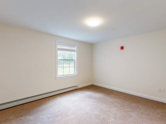 Empty carpeted bedroom with window and baseboard heating at Autumn Woods Apartments, Westbrook
