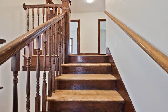 A wooden staircase with a handrail and a mirror at the top.
