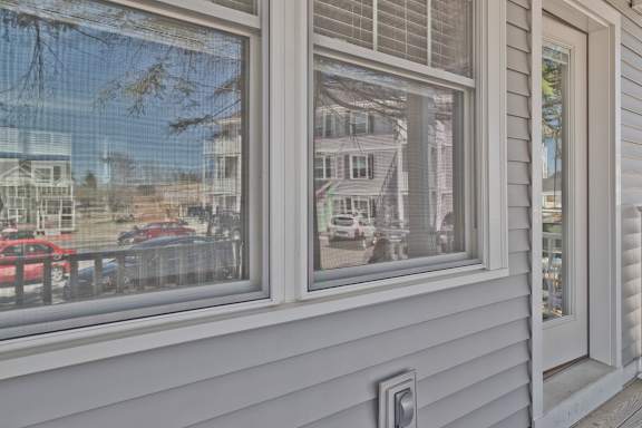 A house with a grey siding and a window reflecting a street scene.
