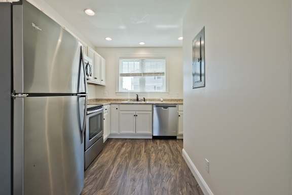 A modern kitchen with a stainless steel refrigerator and wooden flooring.