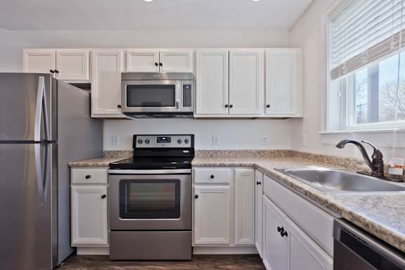 A kitchen with a stainless steel refrigerator, a microwave above the stove, and white cabinets.