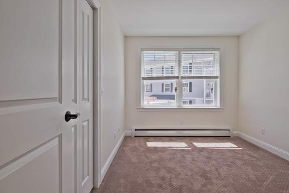 A room with a door, carpet, and a window with a view of a building.