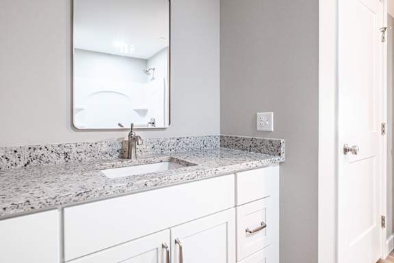 Bathroom vanity with white cabinets and speckled countertop at Windham Village Apartments, Windham