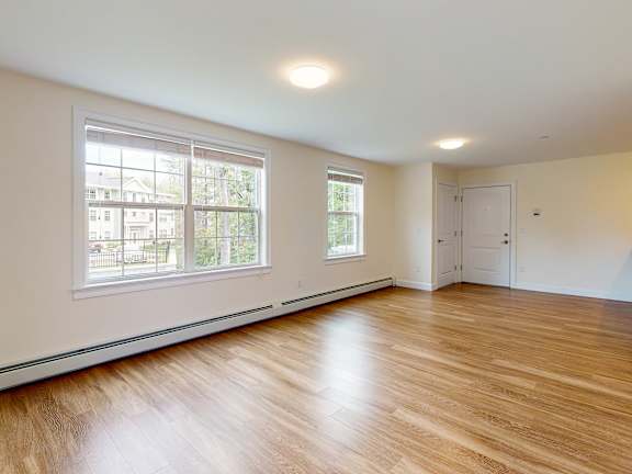 Spacious living room with large windows and entry door at Autumn Woods Apartments, Westbrook, Maine