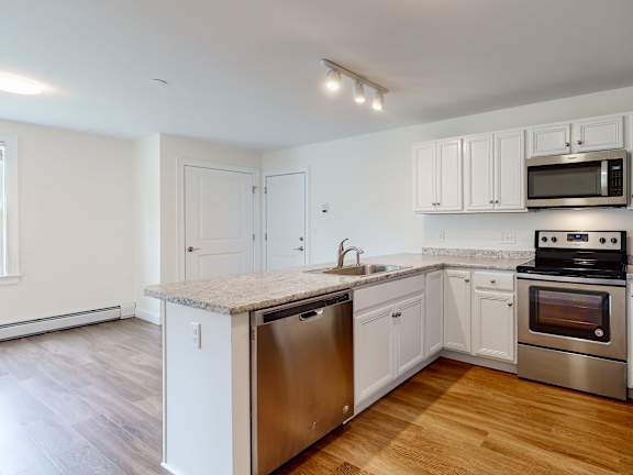 White kitchen with island and stainless dishwasher at Autumn Woods Apartments, Maine