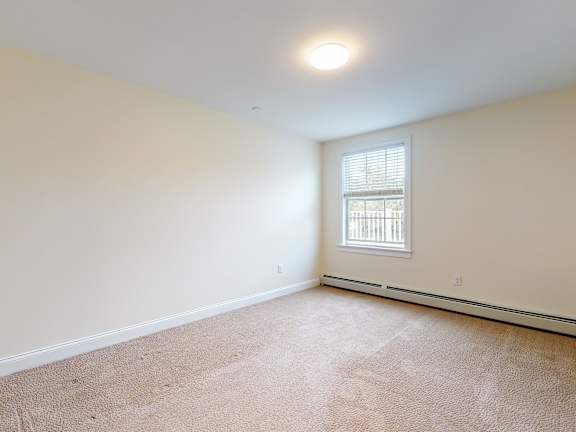 Carpeted bedroom with window and ceiling light at Autumn Woods Apartments, Maine