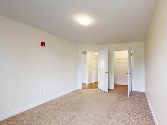 Carpeted bedroom with open closet and hallway view at Autumn Woods Apartments, Westbrook, ME