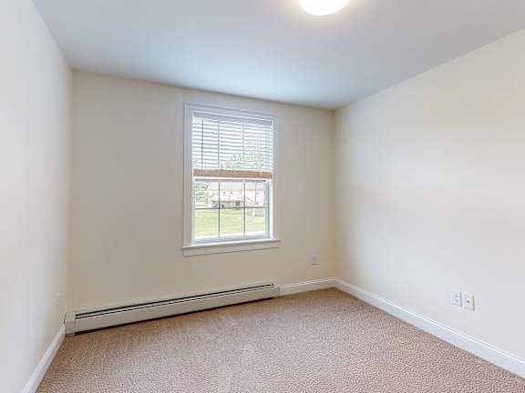 Empty carpeted bedroom with baseboard heating at Autumn Woods Apartments, Westbrook