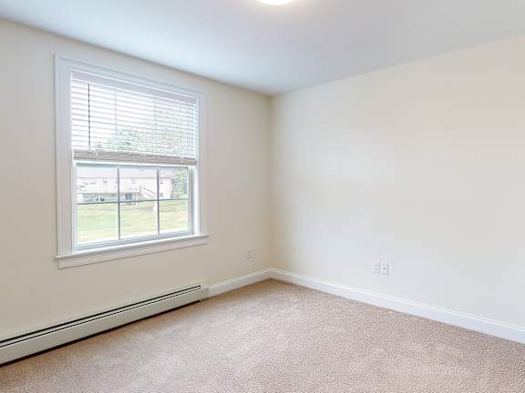 Empty carpeted bedroom with window at Autumn Woods Apartments, Maine
