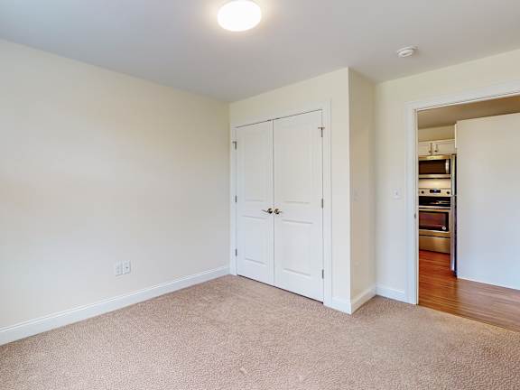 Empty carpeted room with double closet doors at Autumn Woods Apartments, Westbrook, ME