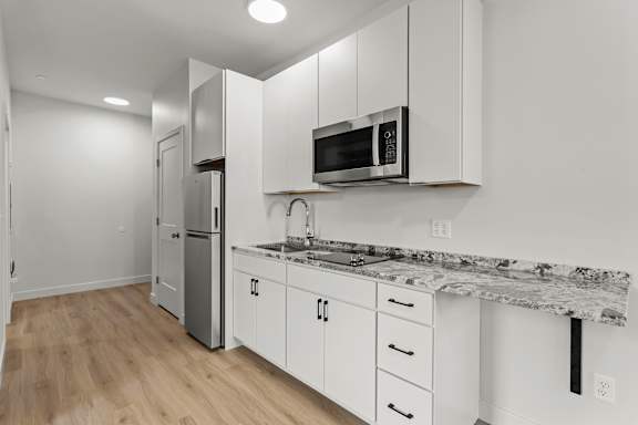 a kitchen with white cabinets and a counter top with a microwave and refrigerator
