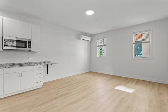 an empty living room with a kitchen and a microwave