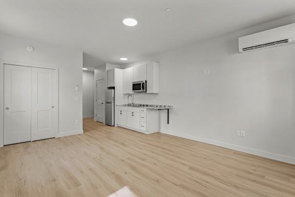 an empty living room and kitchen with white walls and wood flooring