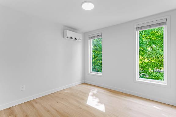 an empty room with two windows and a hardwood floor