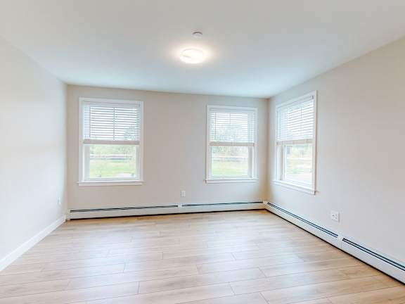 A room with wooden flooring and two windows.
