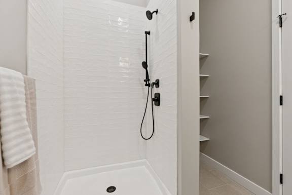 A white tiled shower with a black shower head and hand held shower.