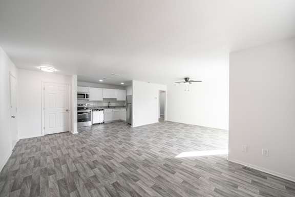 A spacious kitchen and living room with a grey wood floor.